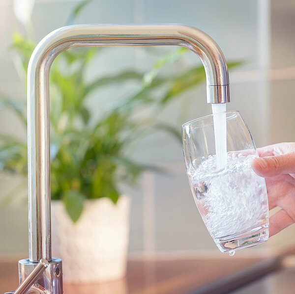 Glas wird am Wasserhahn gefüllt