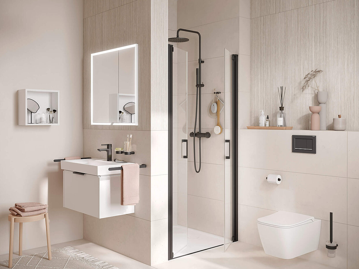 Kleines Bad mit Waschtisch und Lichtspiegel, Dusche und WC. Boden, Wände und Dekoartikel in Pastelltönen. Armaturen und Accessoires in schwarz.