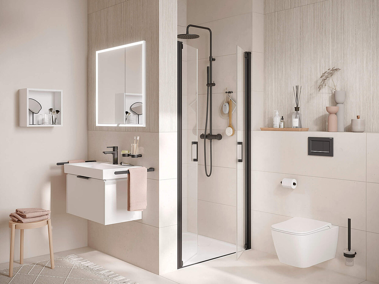 VÉO Kleines Bad mit Waschtisch und Lichtspiegel, Dusche und WC. Boden, Wände und Dekoartikel in Pastelltönen. Armaturen und Accessoires in schwarz.