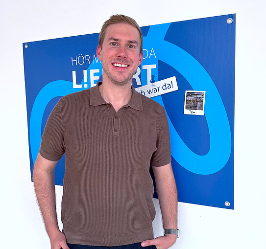 R+F Podcast Gast Tim Braune im Podcast-Studio vor der “Hör mal, wer da liefert”-Fotowand