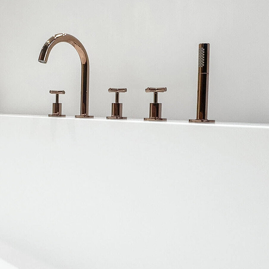 Nahansicht einer farbigen Badewannenarmatur. Von der Badewanne ist nur ein Teil des Randes zu sehen, darauf liegt ein Handtuch. Im Hintergrund eine Dusche mit Glastür und schwarzer Armatur.