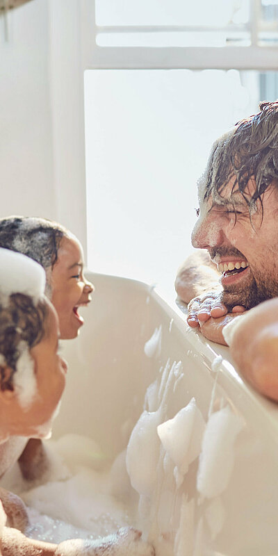 Kinder in Badewanne mit Schaum, Vater davor