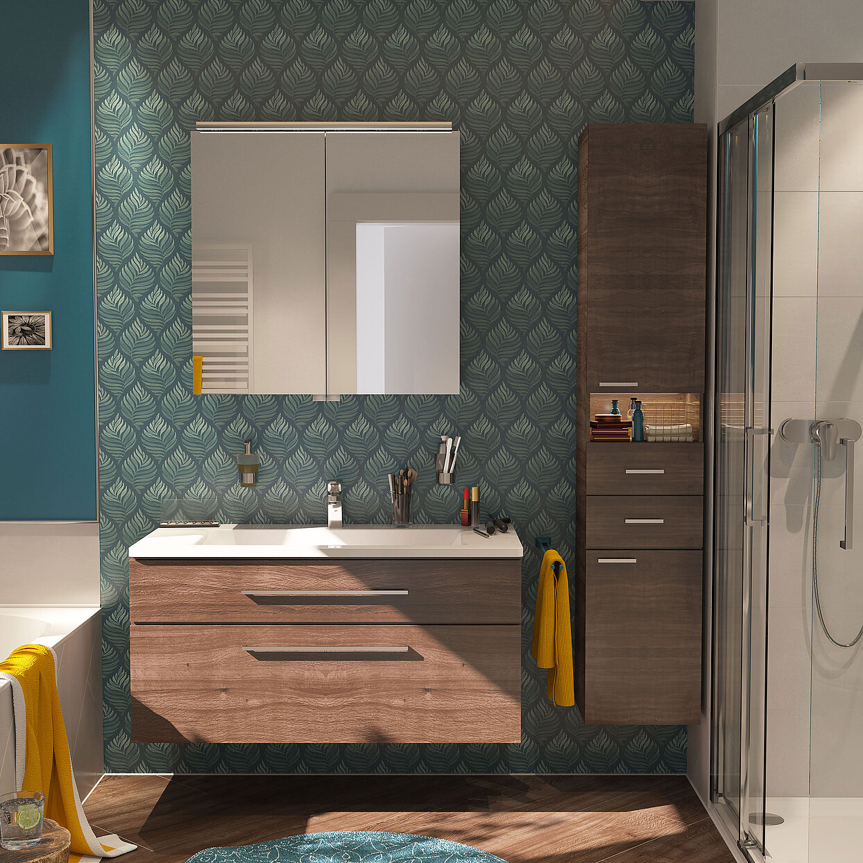 Modernes Badezimmer mit grün-weiß gemustertet Tapete. Im Bildmittelpunkt ein Waschtisch mit Unterschrank in Holzoptik, daruber ein Spiegelschrank. Im Spiegel ist ein weißer Badheizkörper zu sehen. Rechts neben dem Waschtisch steht ein Hochschrank mit Türen, Schubladen und einem offenen Fach, ebenfalls in Holzoptik. Daran anschließend befindet sich eine Dusche mit Duschabtrennung. Am linken Bildrand sieht man noch einen Teil einer Badewanne.